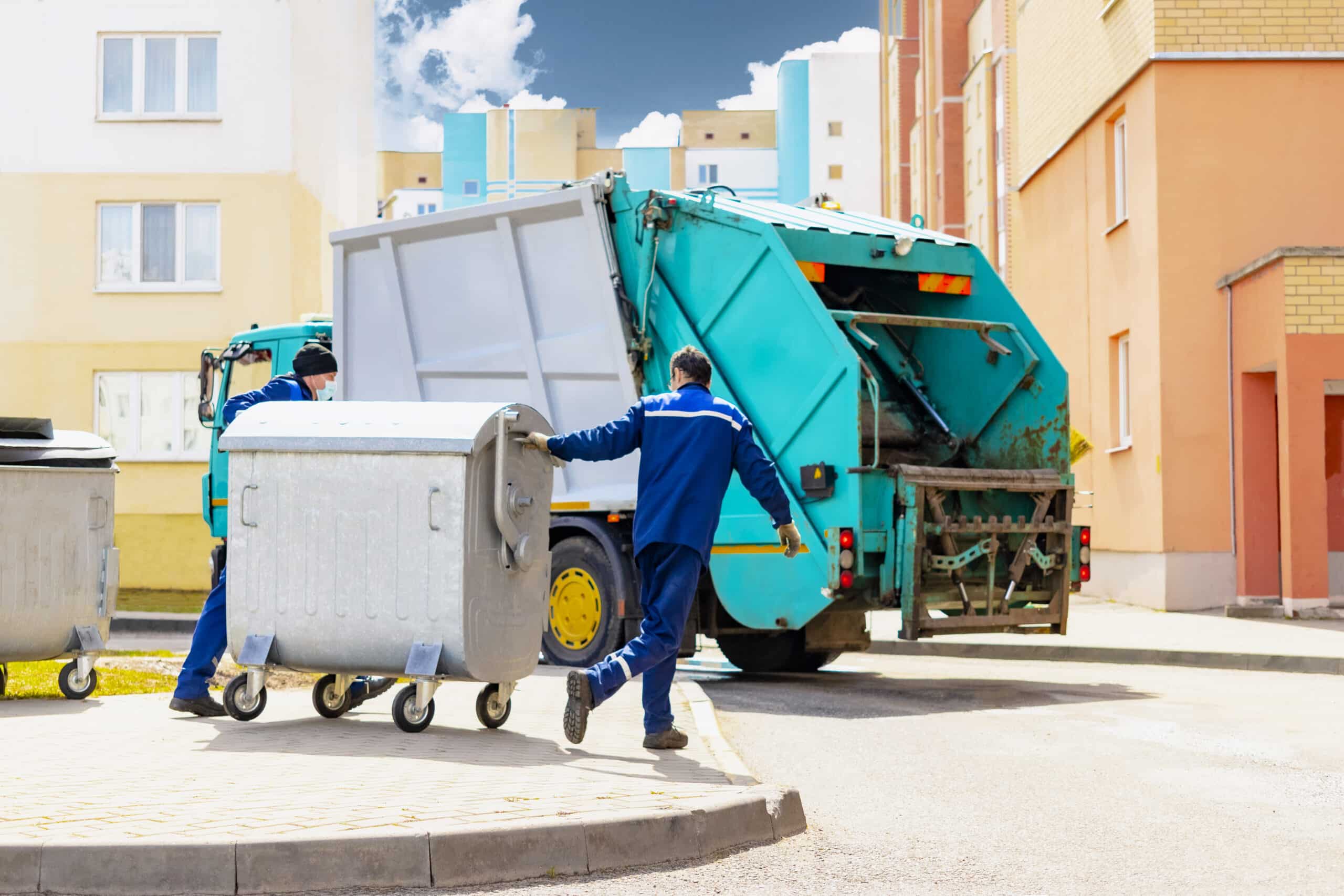An automobile garbage truck collects garbage in residential areas of a modern city. Men load a metal container with garbage into a car for collecting and transporting garbage.